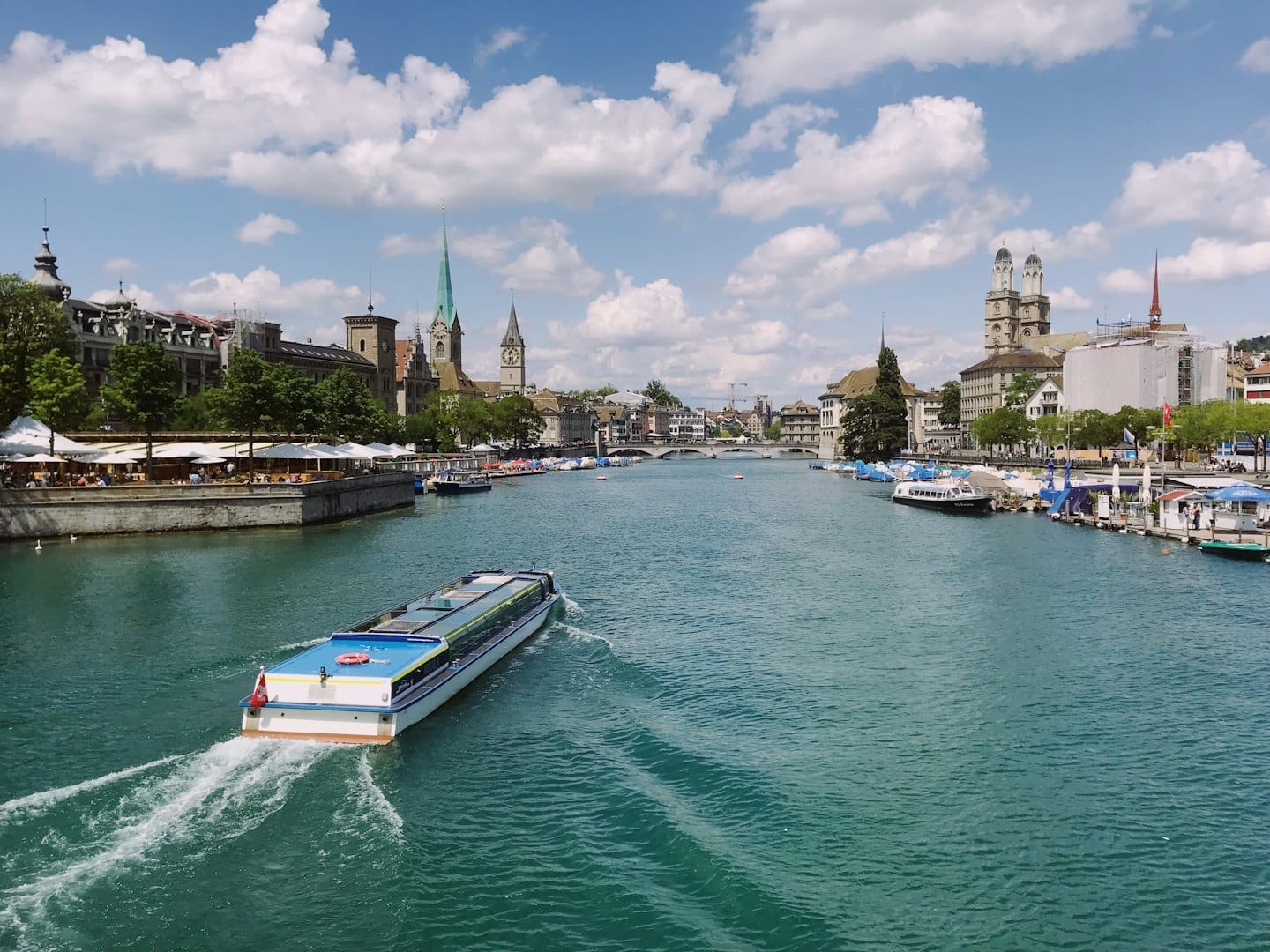 A passenger boat travels down a river lined with European architecture.