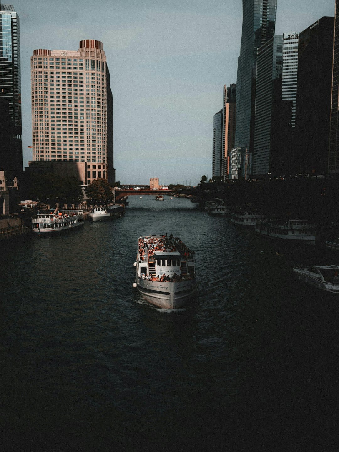 Sightseeing boat carries passengers along an urban river by skyscrapers.