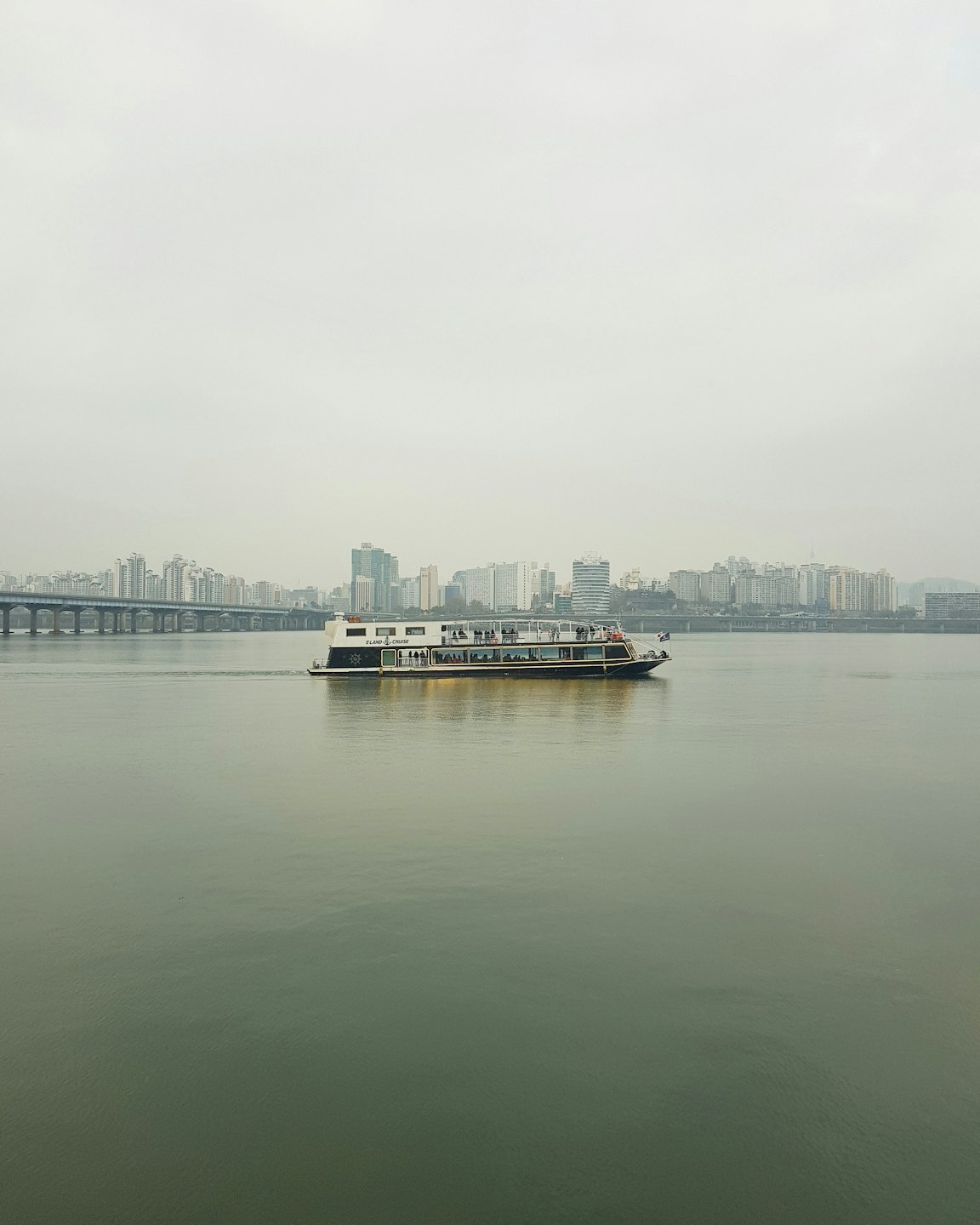 A passenger boat travels on a river near a city skyline.