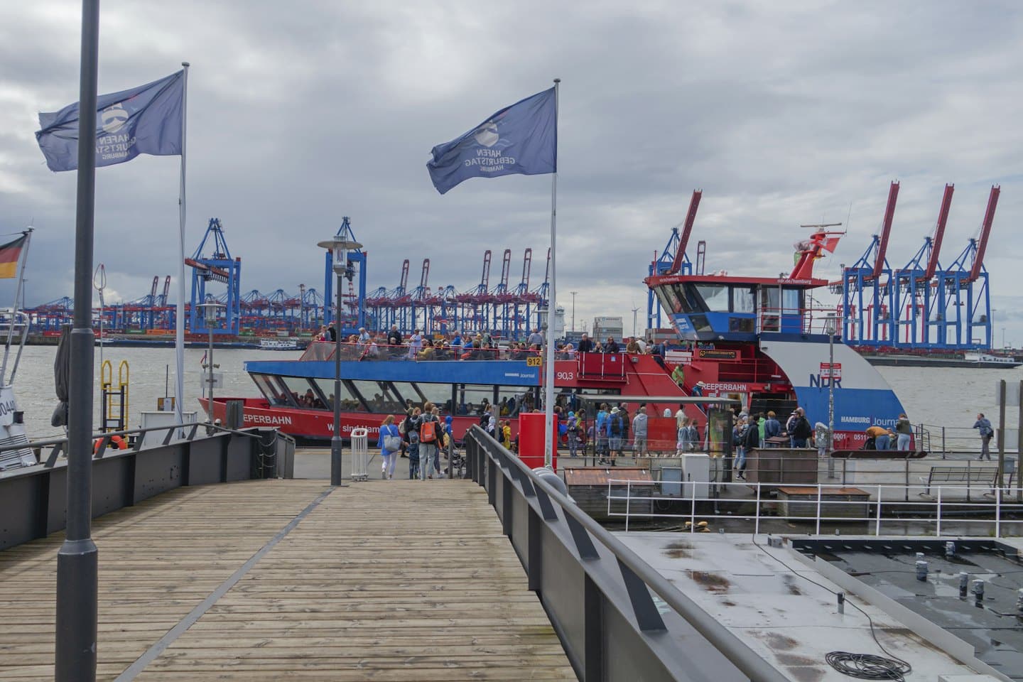 Passengers board a red and blue tour boat at a pier.
